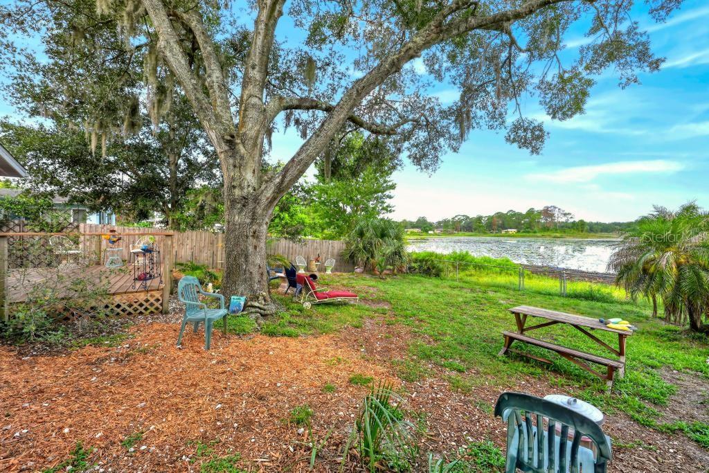 A backyard with a large oak tree, a wooden deck, and a picnic table near water — 37401 TURNER DRIVE, UMATILLA, FL