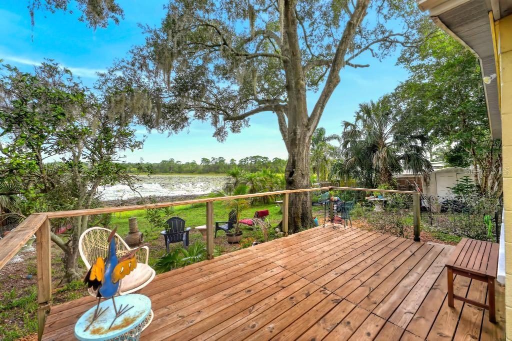 A wooden deck overlooks a backyard with a large tree and a lake in the distance — 37401 TURNER DRIVE, UMATILLA, FL