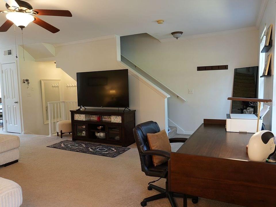A carpeted living room features a television on a stand, a desk, and a staircase — 1004 WATERSIDE DRIVE UNIT 1004, CELEBRATION, FL