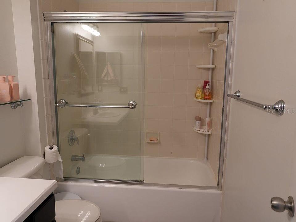 A bathroom features a white bathtub with a sliding glass door and tiled walls — 1004 WATERSIDE DRIVE UNIT 1004, CELEBRATION, FL