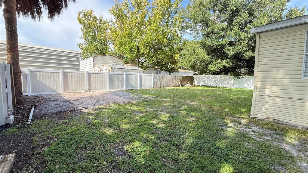 A backyard features a paved patio area, a grassy lawn, and a white vinyl fence — 10404 BRUSSELS DRIVE, RIVERVIEW, FL