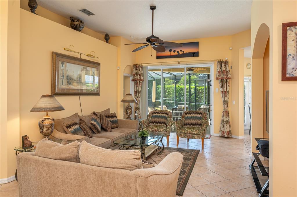 A living room with tile floors, a beige sofa, two patterned armchairs, and sliding doors — 106 SENECA LN, DAVENPORT, FL