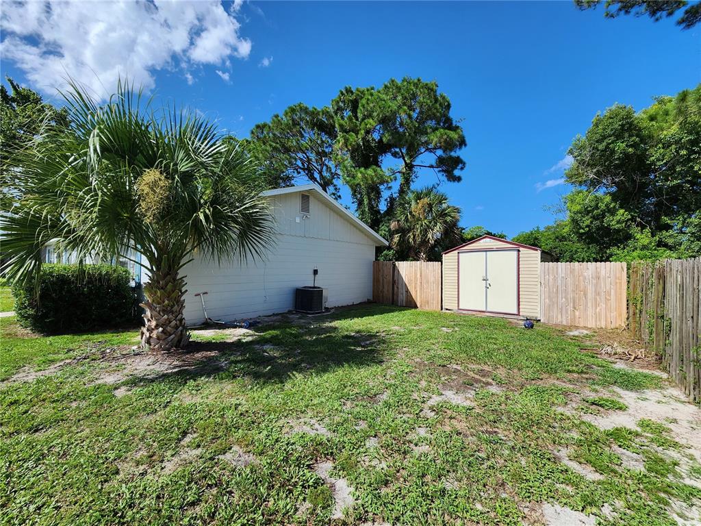 A side view of a house exterior with a palm tree, shed, and wooden fence — 1917 FERN PALM DRIVE, EDGEWATER, FL