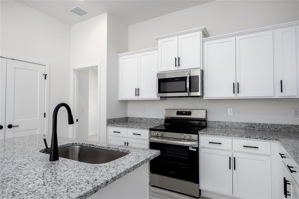 A kitchen features white cabinets, granite countertops, stainless steel appliances, and a black faucet — 16780 NW 178TH TER, ALACHUA, FL