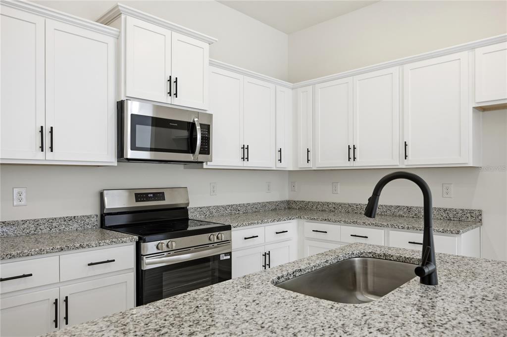 A kitchen features white cabinets, granite countertops, stainless steel appliances, and a black faucet — 16780 NW 178TH TER, ALACHUA, FL