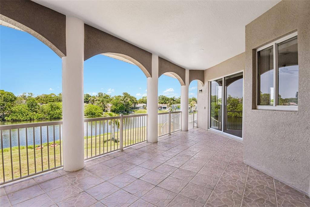 A covered outdoor balcony features tiled flooring, white columns, and a view of a lake — 8335 CHEYENNE DRIVE, SEMINOLE, FL