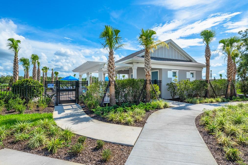 A concrete walkway leads to a community pool building with palm trees and a metal fence — 13729 SQUALL LANE, HUDSON, FL