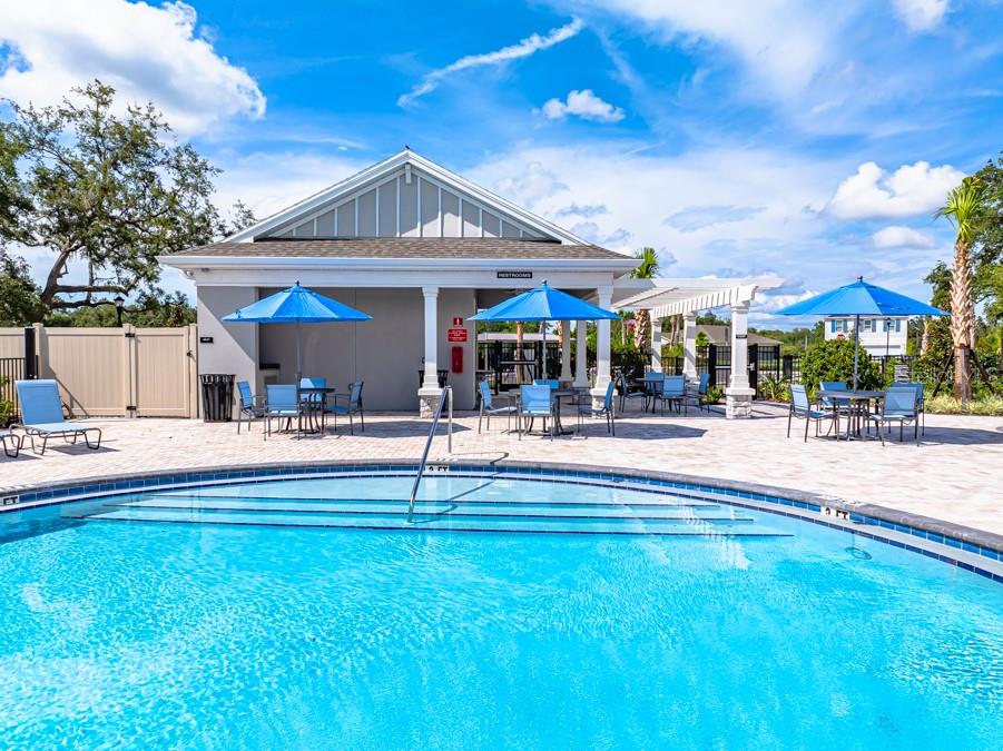 A swimming pool sits in front of a community building with outdoor seating and umbrellas — 13729 SQUALL LANE, HUDSON, FL