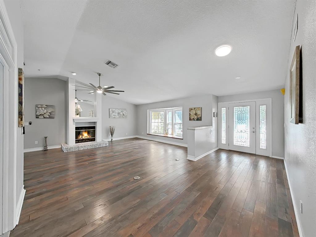 A spacious living room with dark wood flooring, a fireplace, and a front entryway — 438 LAFAYETTE BOULEVARD, OLDSMAR, FL