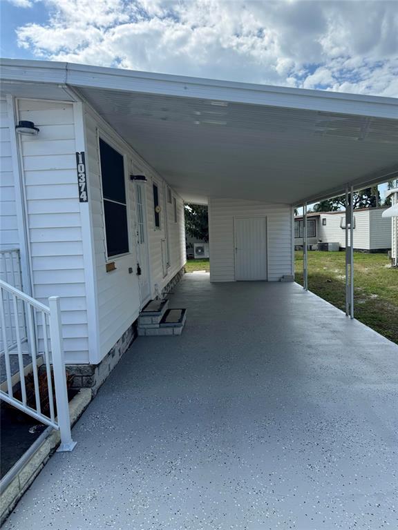 A white mobile home features a covered carport with a gray speckled concrete floor — 10374 106TH AVENUE UNIT 9, LARGO, FL