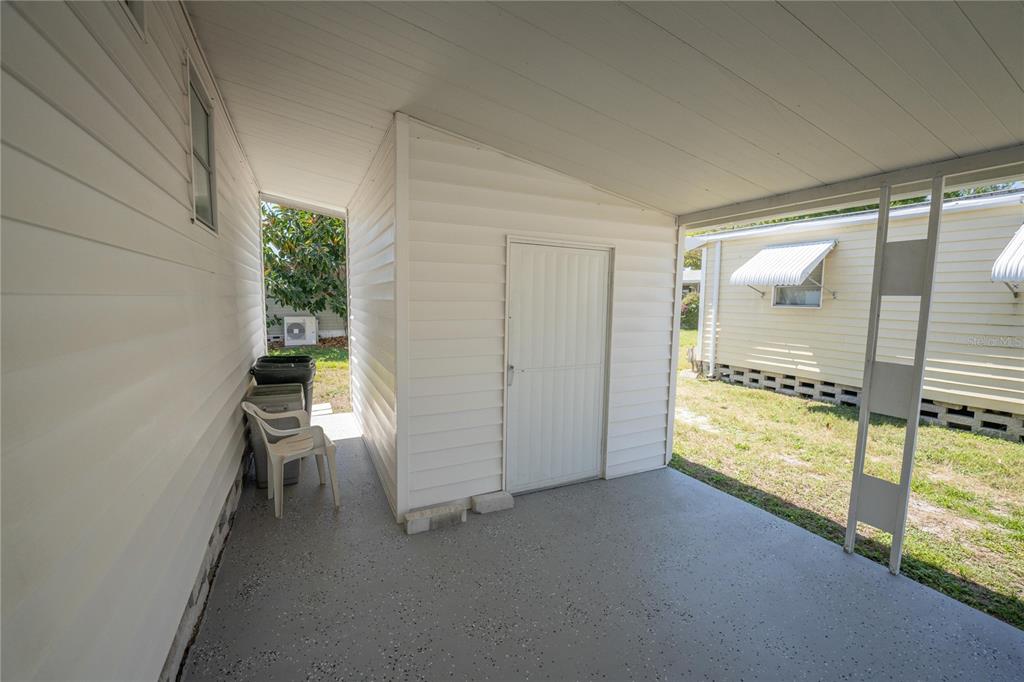 A covered patio area features a white storage shed, concrete flooring, and white siding — 10374 106TH AVENUE UNIT 9, LARGO, FL