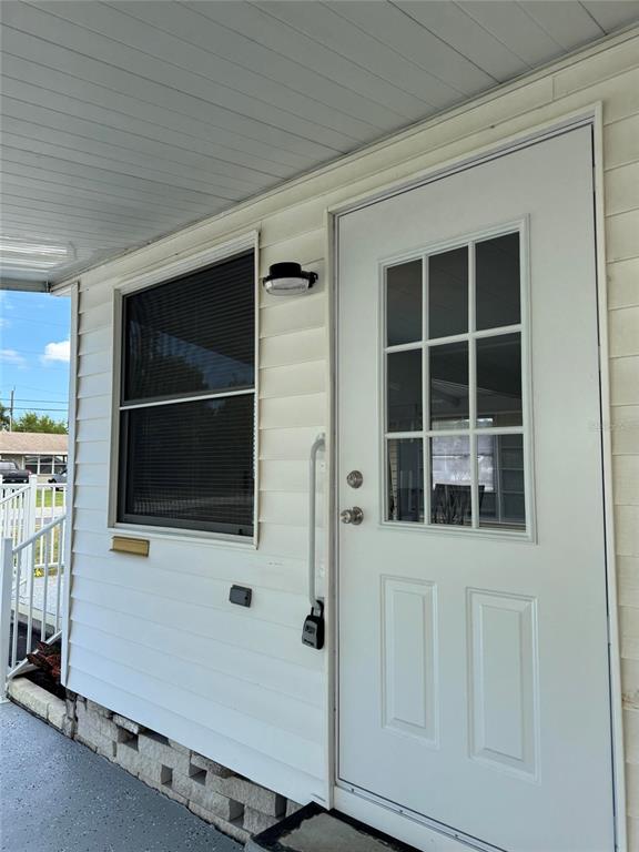 A white exterior door with a glass window panel sits beside a window on a porch — 10374 106TH AVENUE UNIT 9, LARGO, FL