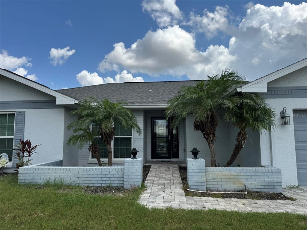 A light-colored brick house features a paved walkway leading to the front door between two palms — 1009 INDIAN HILLS COURT, VENICE, FL
