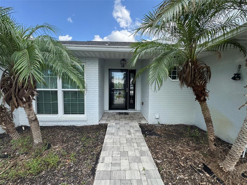 A white brick house exterior features a paved walkway leading to a black front door — 1009 INDIAN HILLS COURT, VENICE, FL