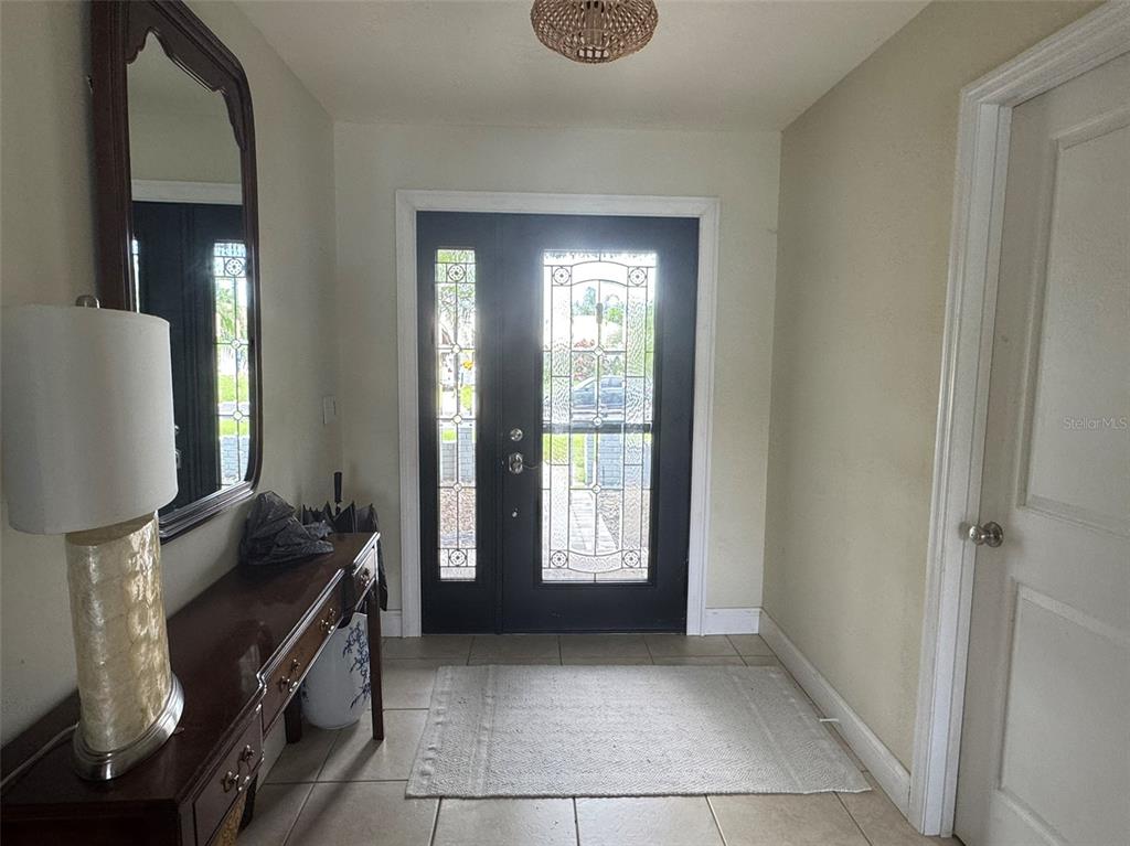 An entryway features a dark double front door, a console table with a lamp, and tile flooring — 1009 INDIAN HILLS COURT, VENICE, FL