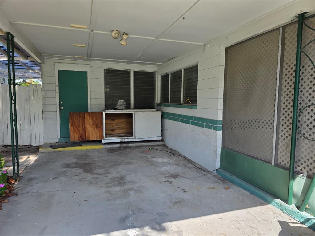 A covered concrete patio features a green door, jalousie windows, and a built-in wooden cabinet — 2015 58TH STREET S, GULFPORT, FL