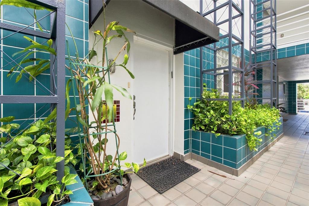 A white front door is framed by teal tiled walls, metal trellises, and potted green plants — 4950 BAYSHORE BLVD UNIT 8, TAMPA, FL