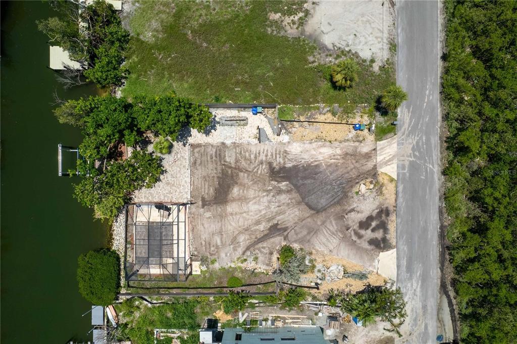 An aerial view shows a vacant waterfront lot with a screened pool enclosure and vegetation — 640 LYONS LANE, LONGBOAT KEY, FL