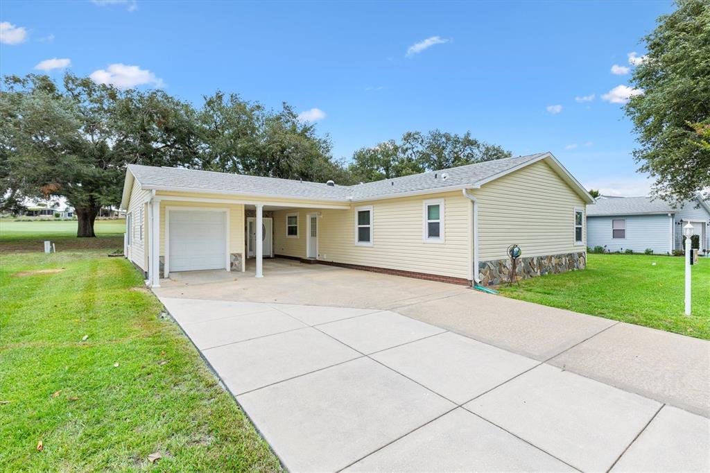 A light yellow single-story house with a carport, concrete driveway, and stone foundation trim — 723 HEATHROW AVENUE, THE VILLAGES, FL