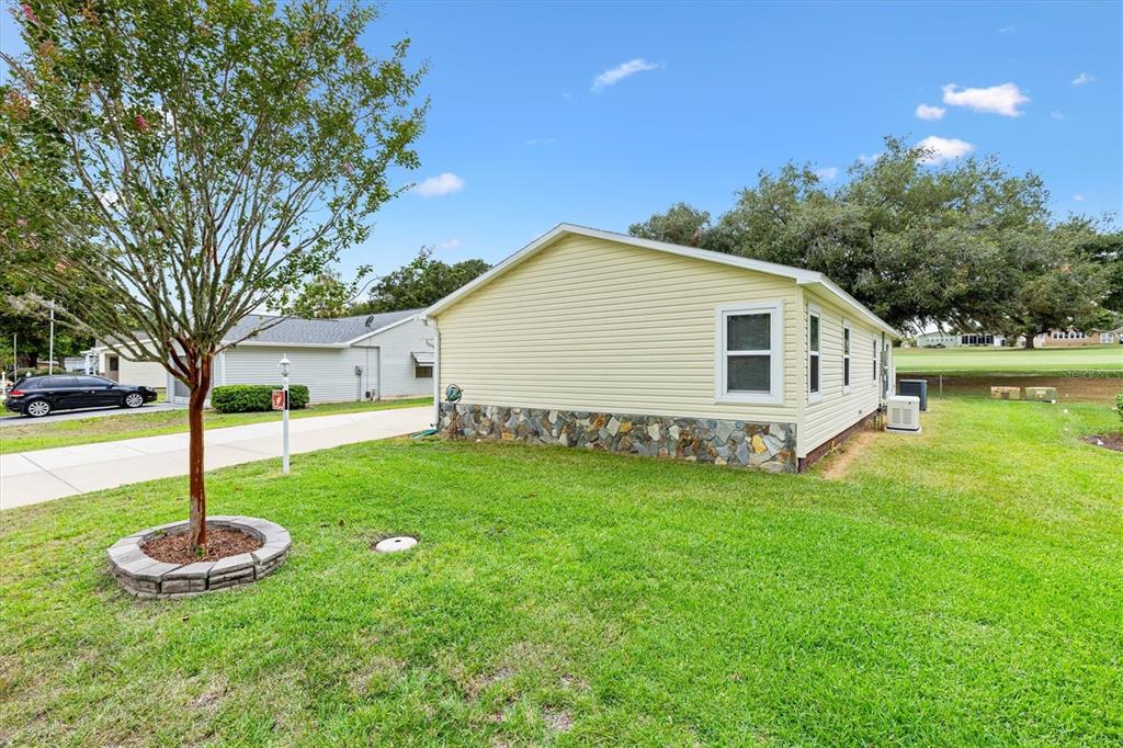 A side view of a light yellow mobile home with a stone-patterned base — 723 HEATHROW AVENUE, THE VILLAGES, FL