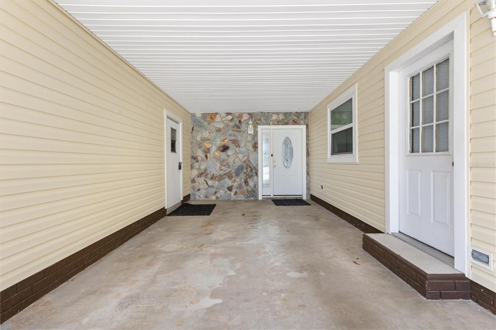 A covered carport with light yellow siding, a stone accent wall, and two white doors — 723 HEATHROW AVENUE, THE VILLAGES, FL
