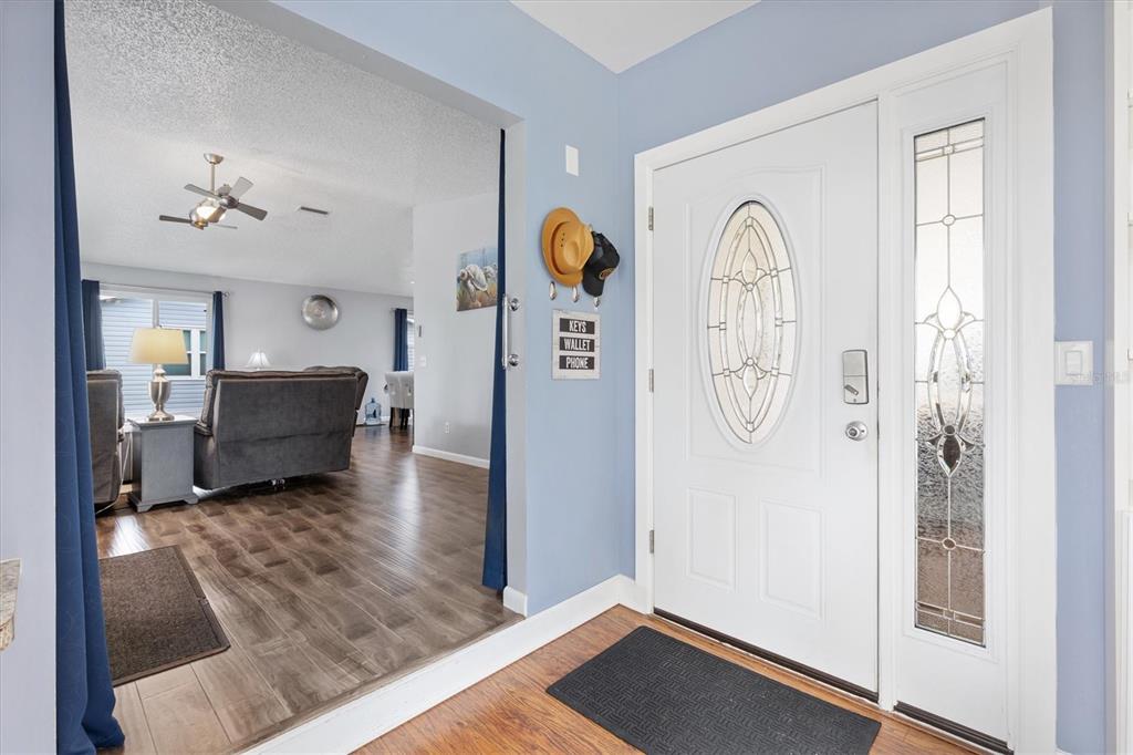 An entryway with a white front door, wood-look flooring, and a view into the living room — 723 HEATHROW AVENUE, THE VILLAGES, FL