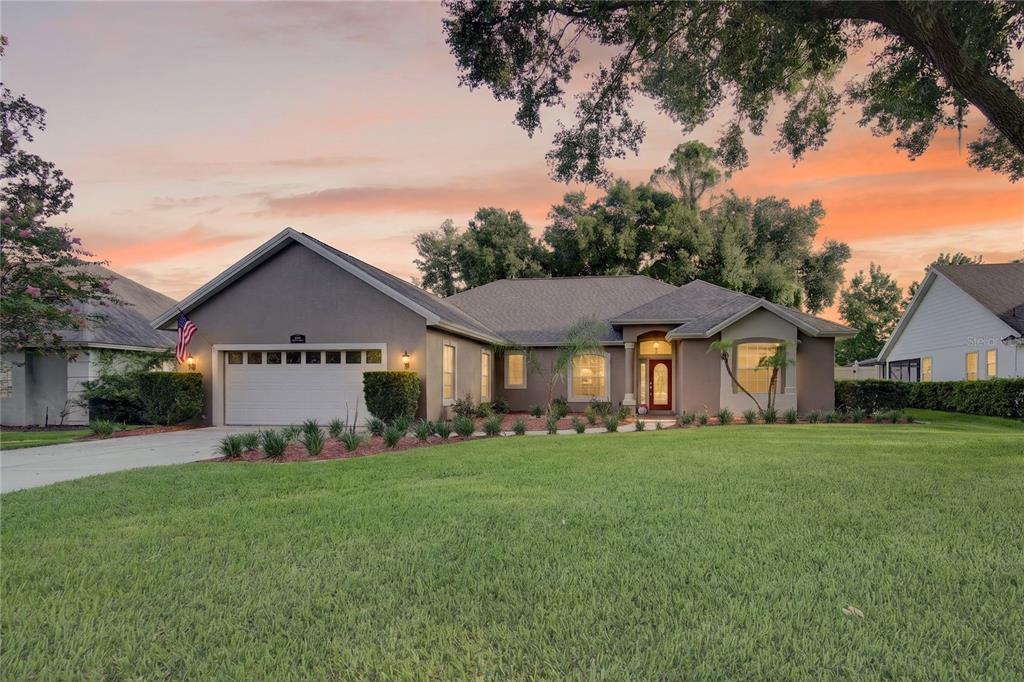 A single-story suburban house with a gray stucco exterior, a two-car garage, and a lawn — 19337 SPRING OAK DRIVE, EUSTIS, FL