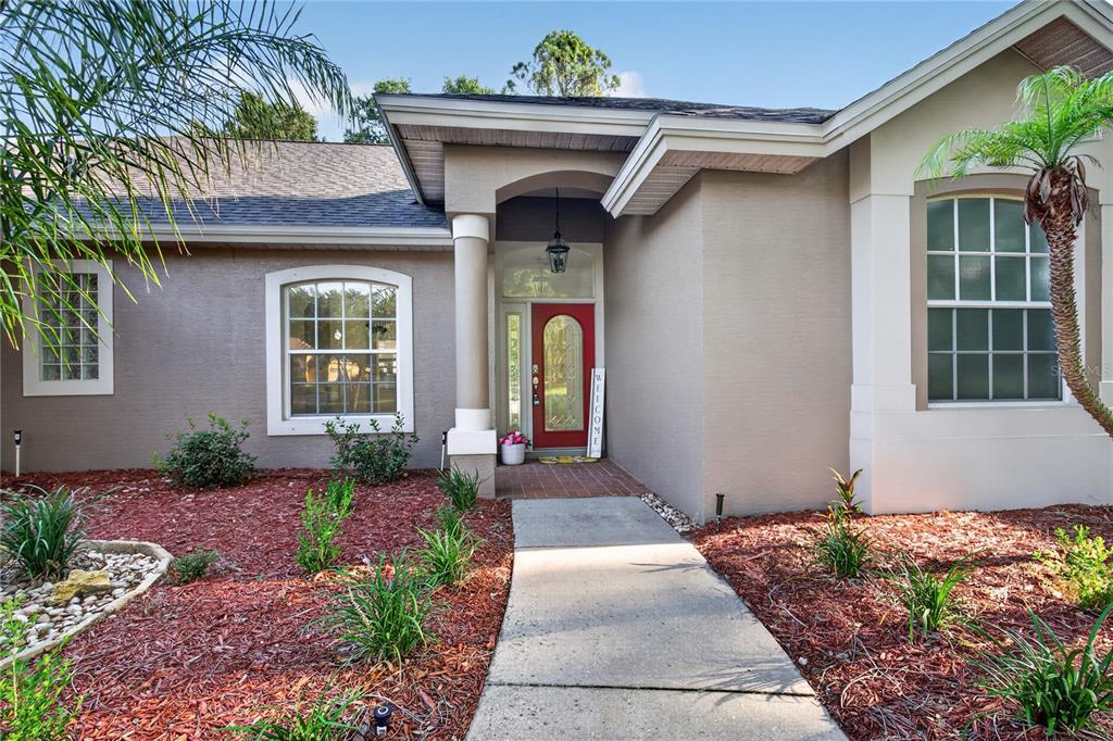 A concrete walkway leads to the red front door of a tan stucco house — 19337 SPRING OAK DRIVE, EUSTIS, FL