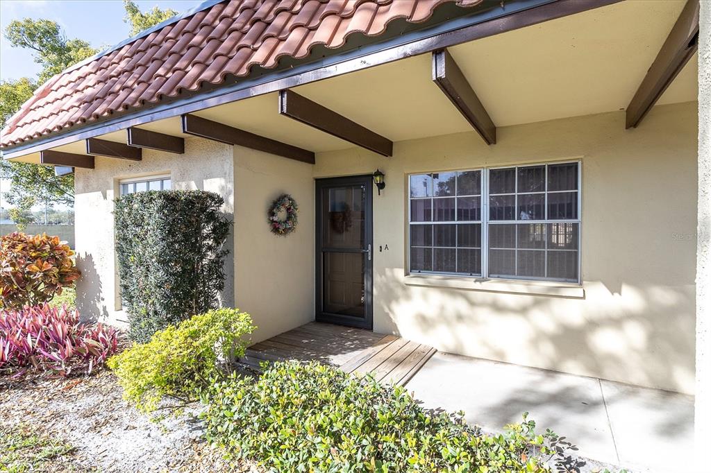 The exterior of a single-story home features a tiled roof, a covered porch, and landscaping — 1701 PINEHURST ROAD UNIT 6A, DUNEDIN, FL