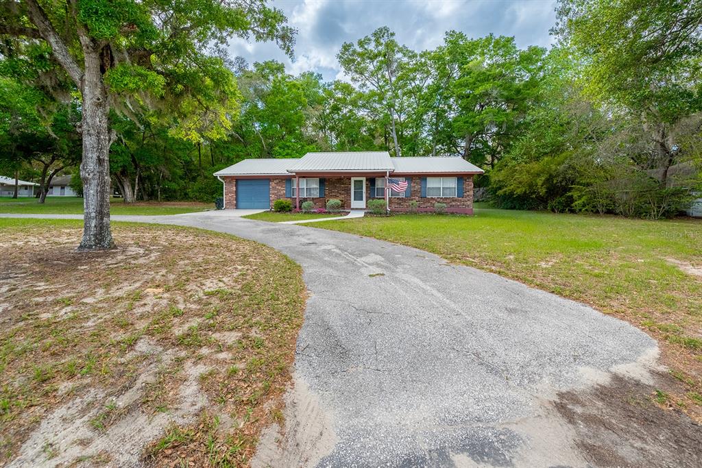 A single-story brick house with a metal roof and a curved asphalt driveway — 102 SWANS NEST CIRCLE, MELROSE, FL