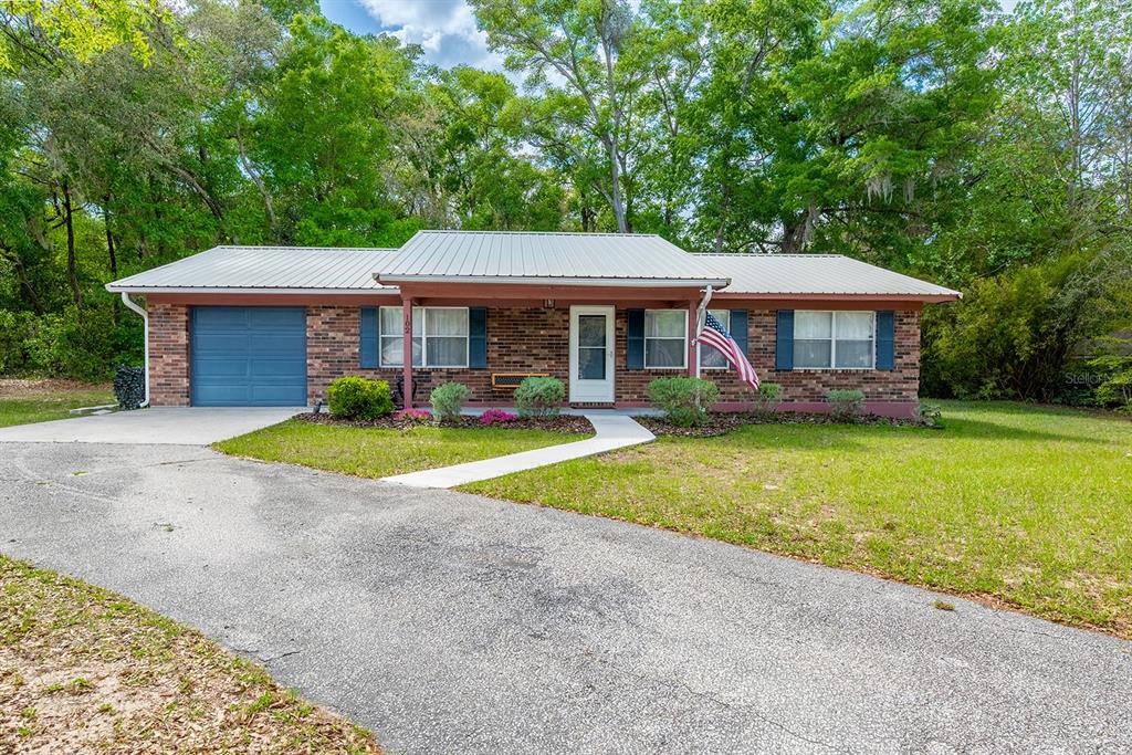 A single-story brick house with a metal roof, attached garage, and front yard — 102 SWANS NEST CIRCLE, MELROSE, FL