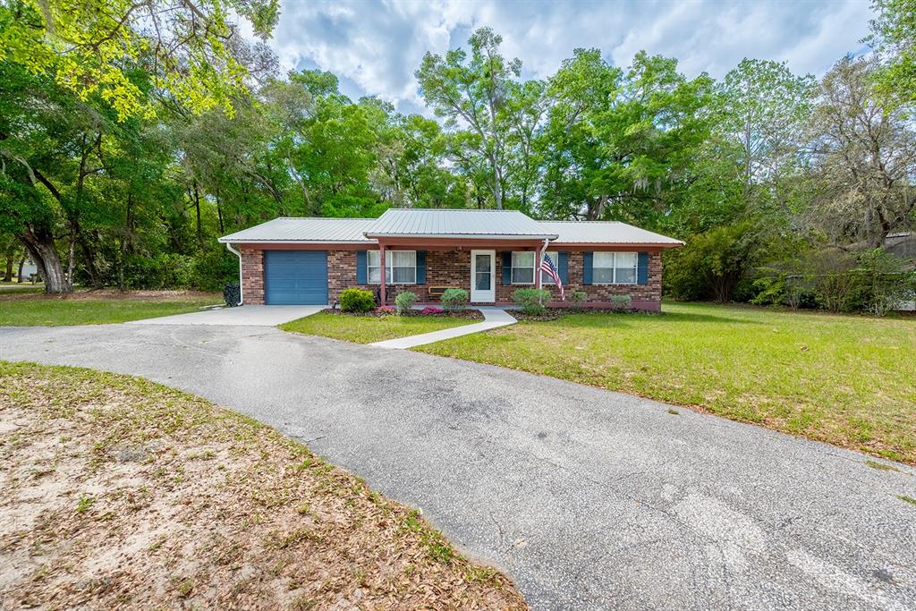 A single-story brick house with a metal roof and a paved driveway sits among trees — 102 SWANS NEST CIRCLE, MELROSE, FL