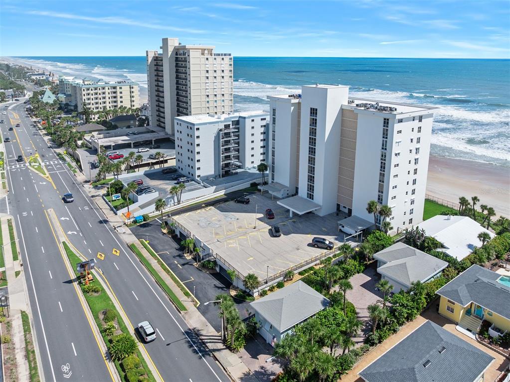 An aerial view shows a coastal road, parking lots, and several multi-story beachfront residential buildings — 111 S ATLANTIC AVENUE UNIT 1104, ORMOND BEACH, FL