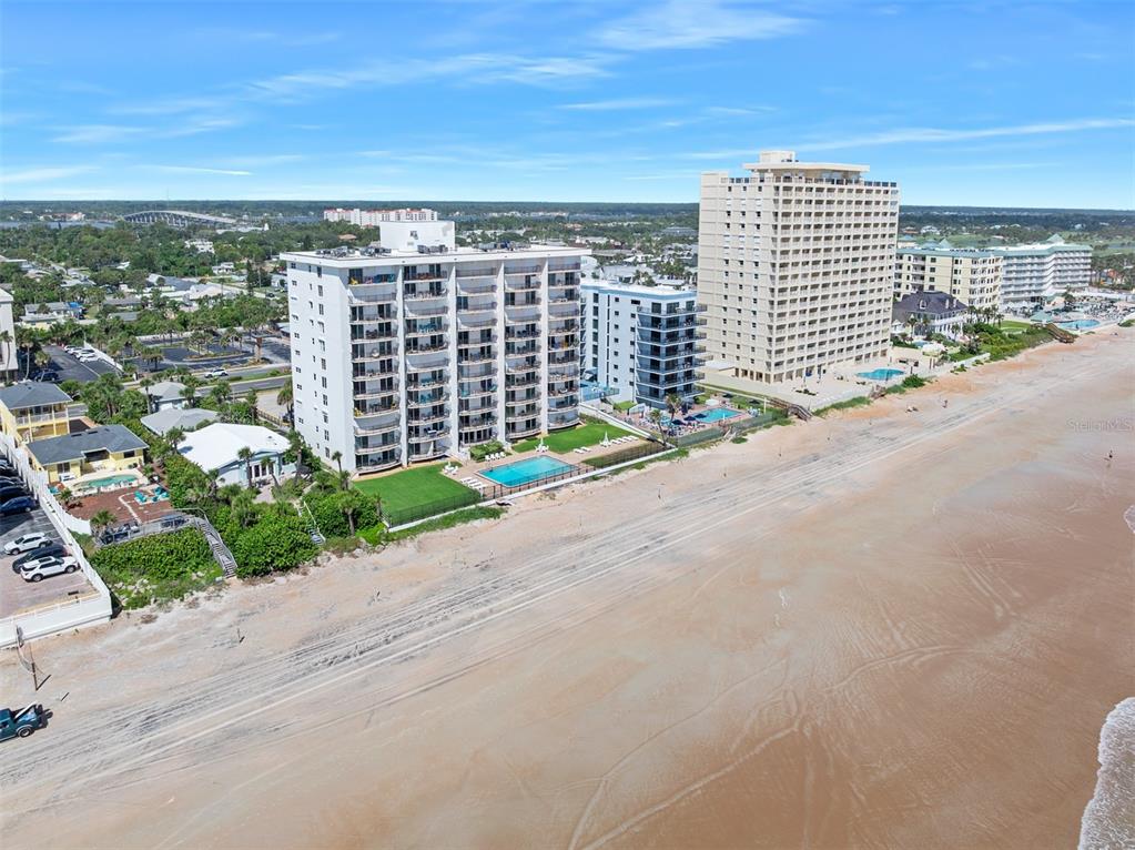 An aerial view shows several high-rise condominium buildings situated directly along a sandy beach — 111 S ATLANTIC AVENUE UNIT 1104, ORMOND BEACH, FL