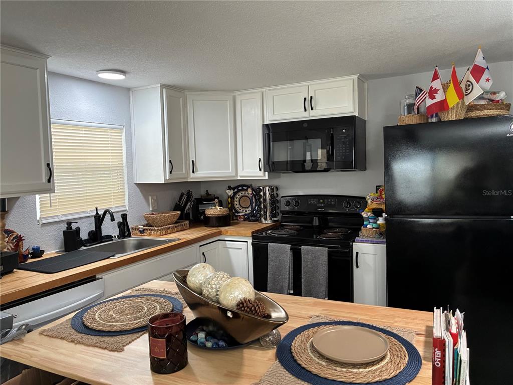 A kitchen features white cabinets, black appliances, and a wooden countertop island with place settings — 30425 TIGER TAIL ROAD UNIT 346, SEBRING, FL