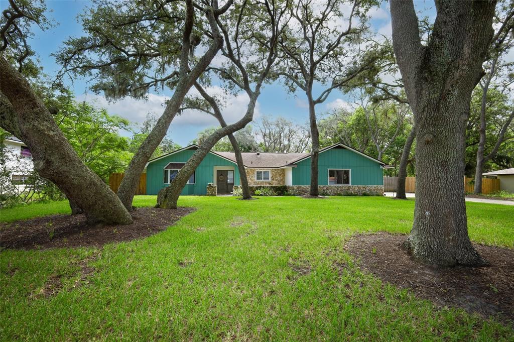 A single-story house with teal siding and stone accents sits behind large oak trees — 1015 ANTELOPE TRAIL, WINTER SPRINGS, FL