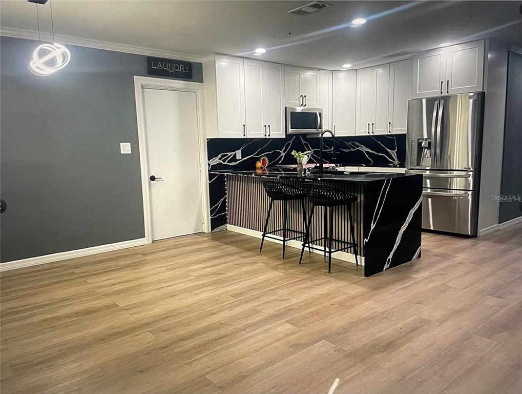 A kitchen features white cabinets, black marble-patterned countertops, and a breakfast bar with two stools — 1929 3RD AVENUE E, BRADENTON, FL