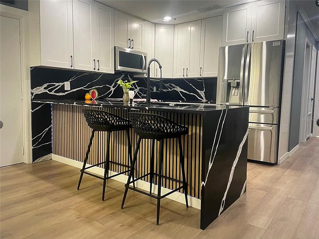 A kitchen features white cabinets, black marble countertops, a slatted wood island, and two stools — 1929 3RD AVENUE E, BRADENTON, FL