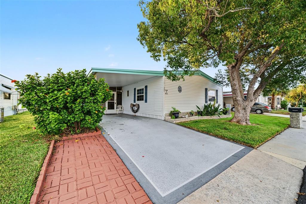A single-story mobile home features a carport, a brick walkway, and a large shade tree — 3207 BREWSTER DRIVE, HOLIDAY, FL