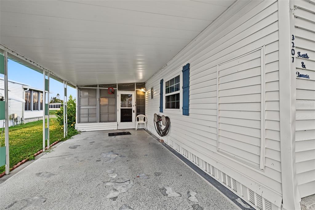 A covered concrete carport leads to the entrance of a white mobile home — 3207 BREWSTER DRIVE, HOLIDAY, FL