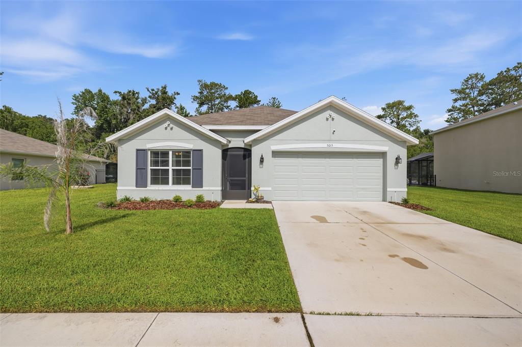 A single-story house with a light green exterior, a two-car garage, and a front lawn — 5015 CADIZ COURT, BROOKSVILLE, FL