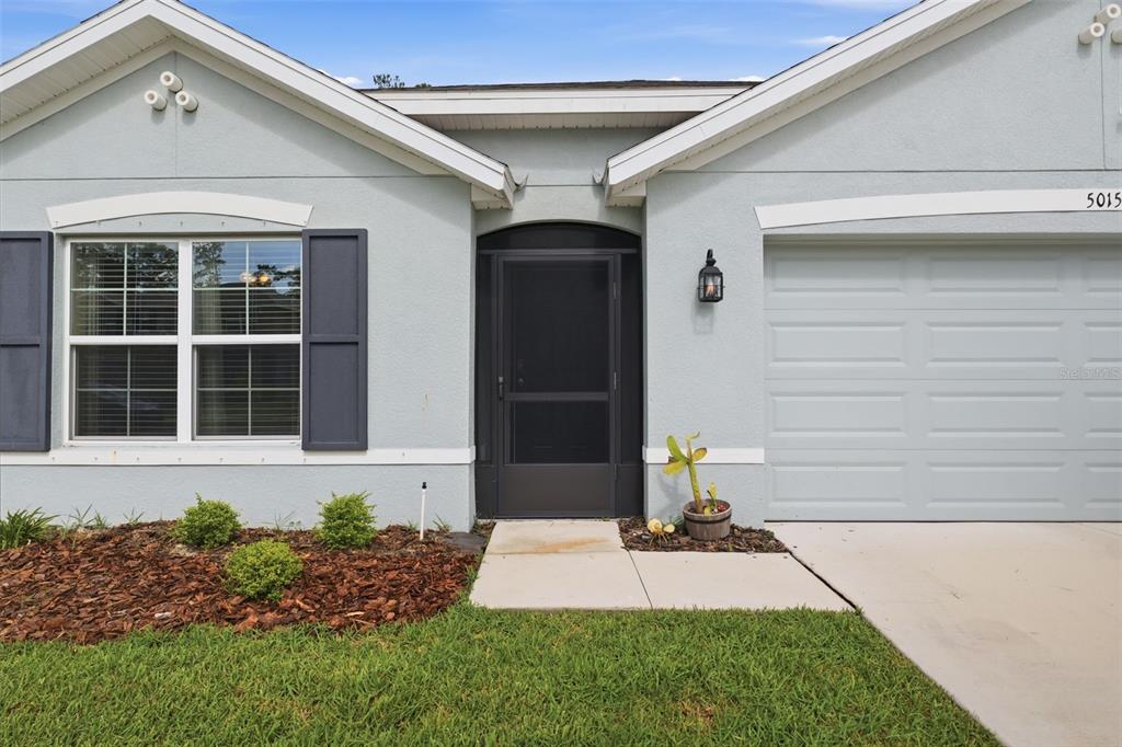 The exterior of a light blue house features a garage, a front door, and landscaping — 5015 CADIZ COURT, BROOKSVILLE, FL