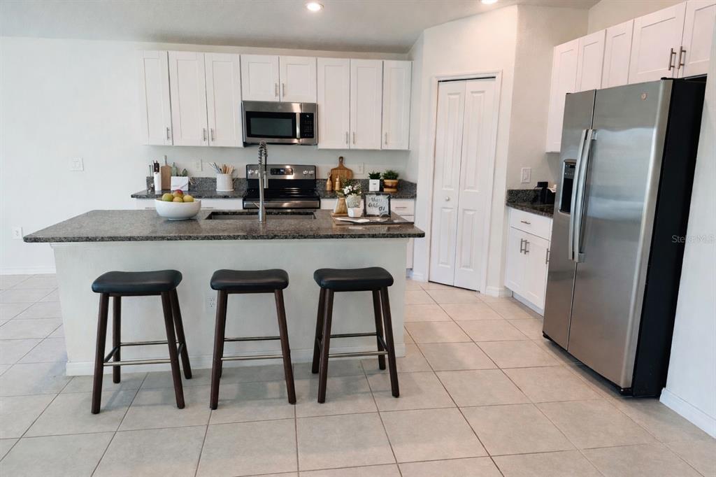A kitchen features white cabinets, granite countertops, a stainless steel refrigerator, and a breakfast bar — 13181 GARNET RASPBERRY AVENUE, WIMAUMA, FL
