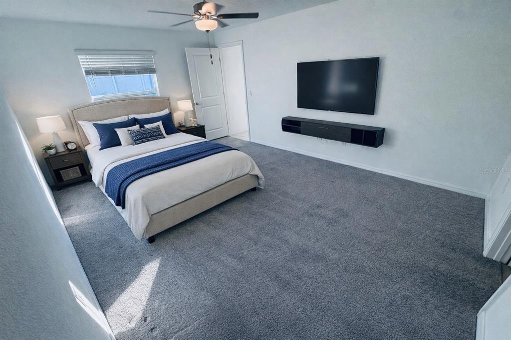 A bedroom features a bed with blue bedding, a wall-mounted television, and gray carpeting — 13181 GARNET RASPBERRY AVENUE, WIMAUMA, FL