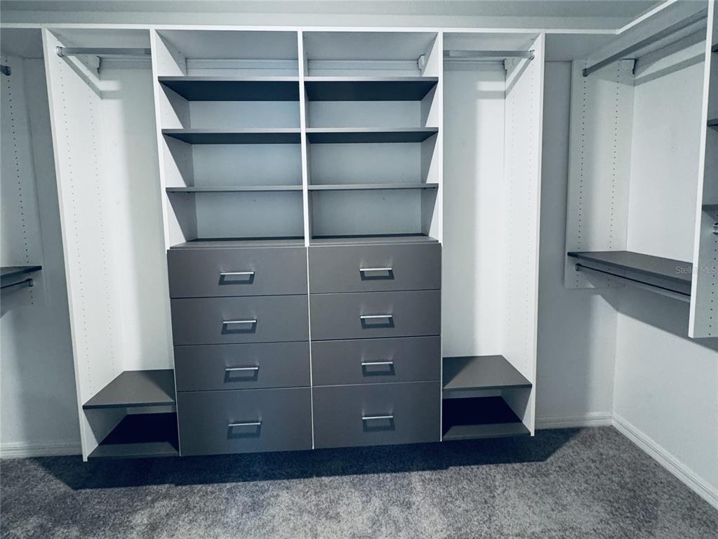 A walk-in closet features white shelving, grey drawers, and hanging rods on a grey carpet — 13181 GARNET RASPBERRY AVENUE, WIMAUMA, FL