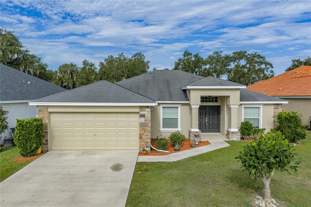 A single-story suburban house with a tan stucco exterior, stone accents, and a two-car garage — 4505 FAIRWAY OAKS DRIVE, MULBERRY, FL