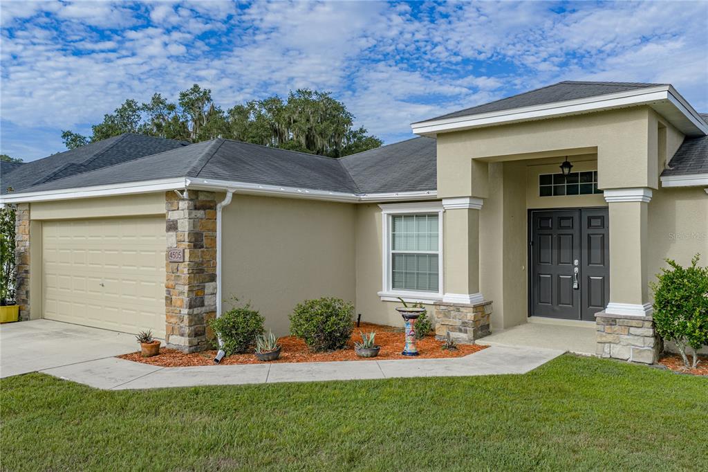A single-story house exterior features a tan stucco facade, stone accents, and a double front door — 4505 FAIRWAY OAKS DRIVE, MULBERRY, FL