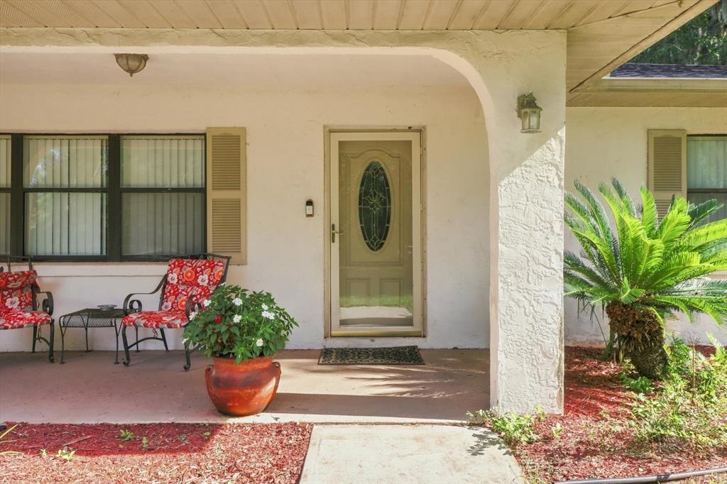 A covered front porch features a glass-paneled door, two chairs, and a potted plant — 9685 W TOM MASON DRIVE, CRYSTAL RIVER, FL