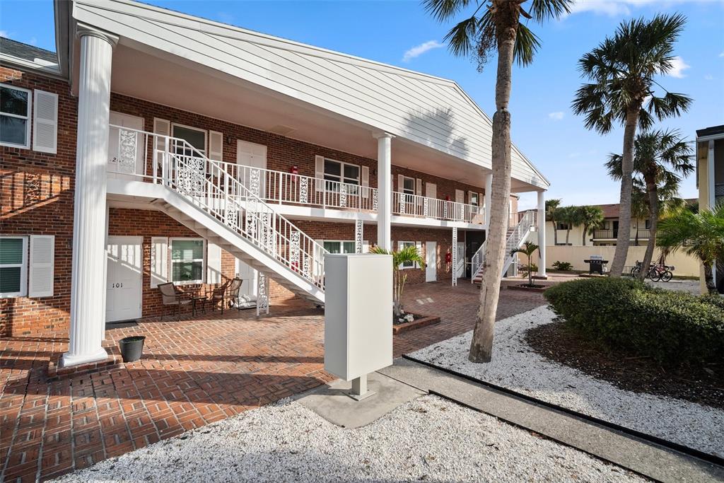 A two-story brick apartment building features white railings, exterior staircases, and a paved courtyard — 380 BASE AVENUE E UNIT 202, VENICE, FL