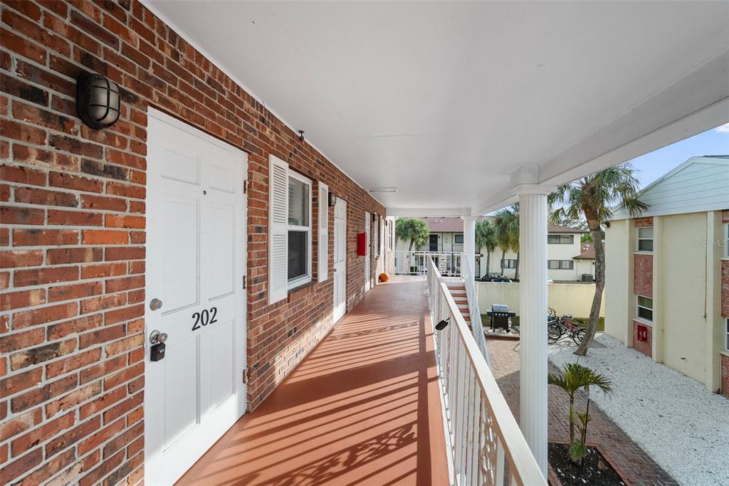 An outdoor walkway with brick walls, white doors, and a covered balcony overlooking a courtyard — 380 BASE AVENUE E UNIT 202, VENICE, FL